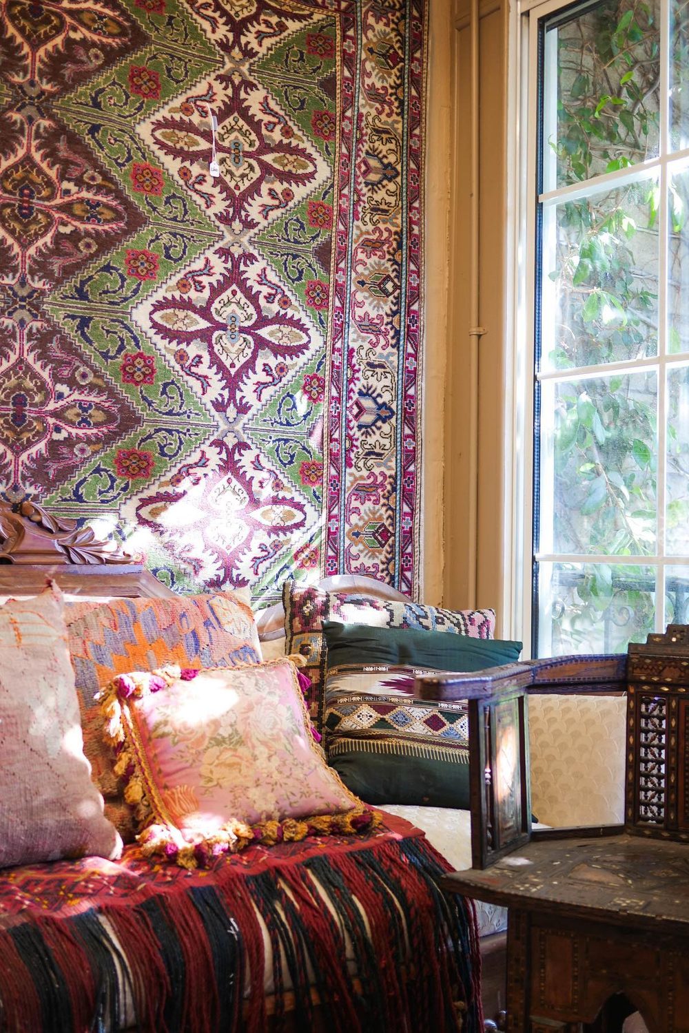 A gallery room layered with antique rugs, pillows and painted chests